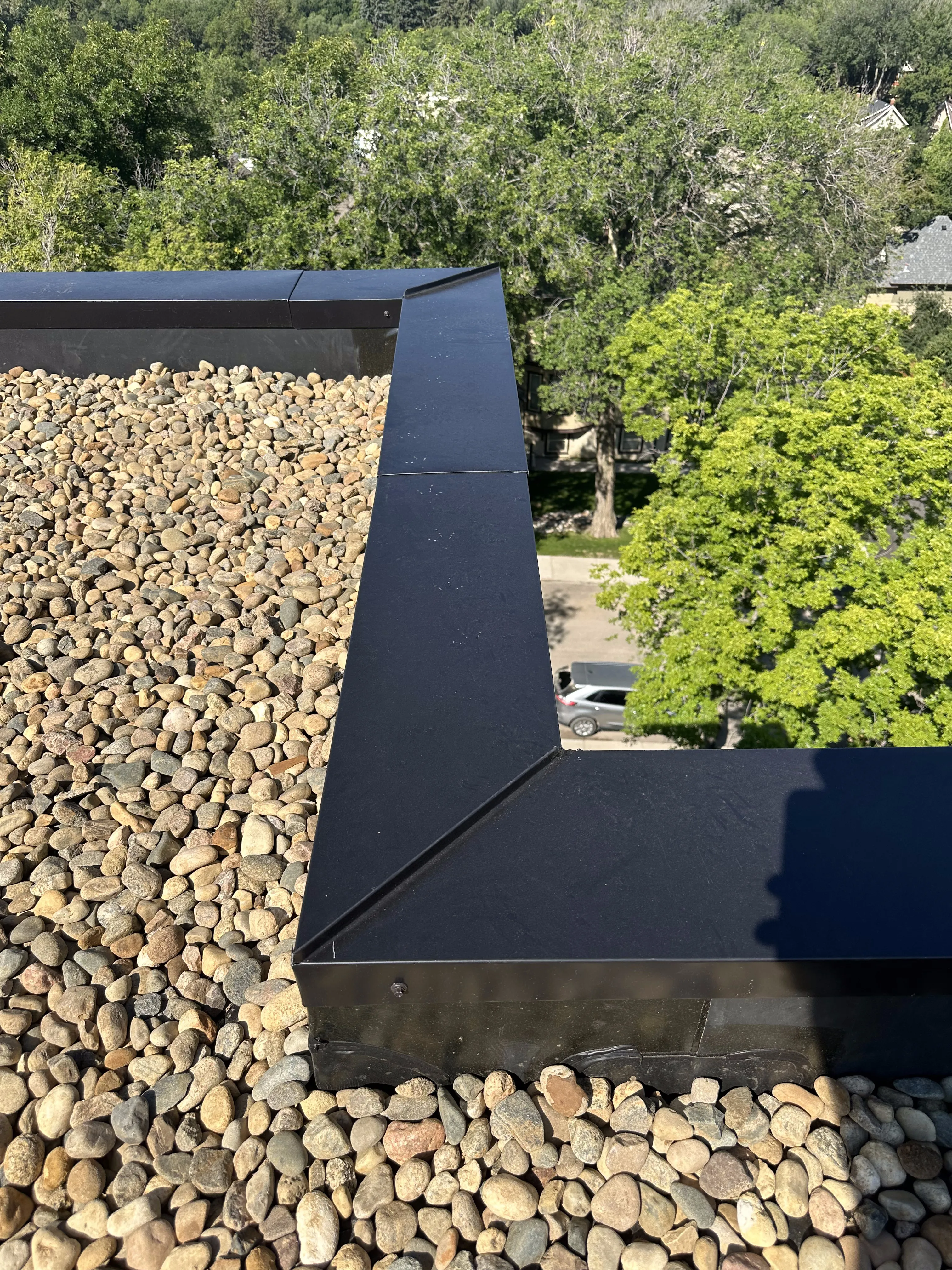 Finished flat roof with river rock ballast and black metal coping in Calgary